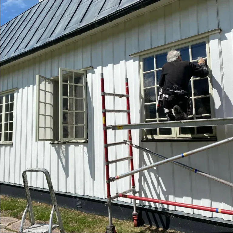 Målare renoverar fönster på Öje kapell från en ställning