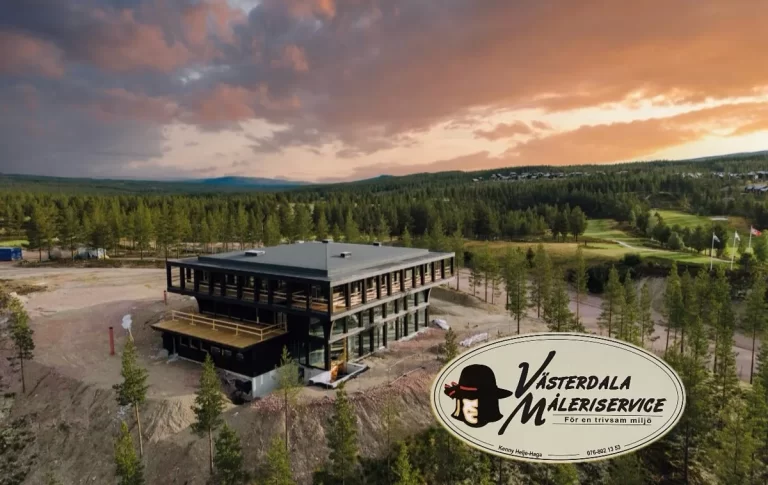 Mörk hotellbyggnad med trädäck och stora fönster bland tallar, golfbana och solnedgång i bakgrunden